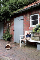 Boy sitting on garden bench next to wooden crates outside brick house