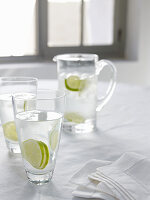 Carafe and glasses of water with lime slices in front of window