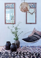 Floor vases and metal armchairs with cushions on rag rug below vintage mirrors on the wall