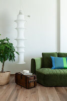 Pendant lamp above old wooden chest between green upholstered sofa and house plant