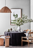 Vase mit Blütenzweigen auf rundem Tisch mit lila Tischdecke, Hocker und Stühle, moderne Kunst and der Wand