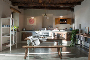 Rustic table and bench and crockery on shelves in kitchen with wood-beamed ceiling