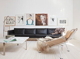 Schwarzes Ledersofa, darüber Kunstwerke, Couchtisch mit Marmorplatte und Designerstuhl in hellem Wohnzimmer