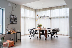 Dining area in front of floor-to-ceiling windows with curtain in open-plan living room