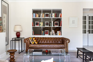 Brown leather couch and acrylic glass table in front of shelves in living room