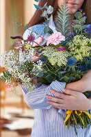 Woman holding bouquet of carnations, gypsophila, wild carrot, veronica, globe thistle, astrantia and eucalyptus