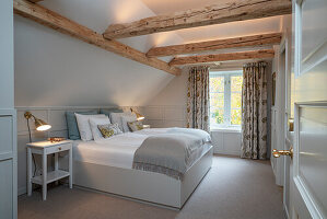 Double bed in a bedroom with sloping roof and wooden beams with LED lighting