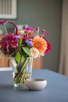 A bouquet of dahlia in a glass vase, and a porcelain bowl on a table
