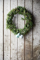 Wreath made of juniper branches with Christmas baubles on a board wall