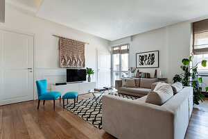 Pale sofa set, TV cabinet, woollen wall-hanging and turquoise chair with footstool in living room