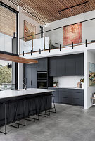 Long kitchen island with bar stools and black kitchen cabinets below gallery level