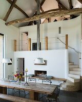 Beamed ceiling in converted barn with double height, refectory style table and gas fireplace