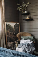 Vintage French chair with blankets, behind it landscape painting in the bedroom with dark walls