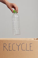 Child's hand placing plastic bottle in cardboard box for recycling