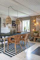 Dining table with rattan armchairs on black and white carpet, above boho hanging lights