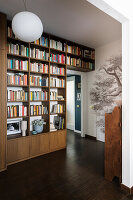 Floor-to-ceiling bookshelves and mural wallpaper with tree motif in hallway