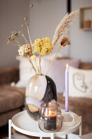 Glass vase with dried flowers, candle and lantern on side table