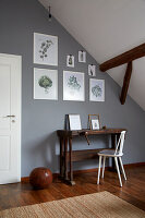 Rustikaler Arbeitstisch mit Stuhl an grauer Wand mit botanischen Zeichnungen