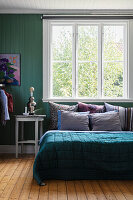 Double bed with scatter cushions and quilt in bedroom with green-painted wooden wall