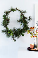 Christmas wreath on white wall with decorative plate and candle on side table