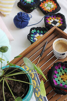 Colourful crocheted squares next to wooden tray with coffee mug and houseplant