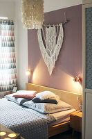 Double bed below sconce lamps and macramé wall-hanging in bedroom