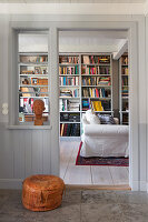 Blick ins Zimmer mit raumhohem Bücherregal und Hussensessel, im Vordergrund Lederpouf