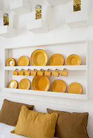 Tellerregal mit gelben Tellern und Tassen, darunter Sitzbank mit farblich passenden Kissen