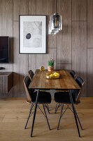 Dining table with four chairs in front of wood panelling in open-plan living area