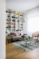 Blick ins Wohnzimmer mit raumhohem Bücherregal, Sofa und Couchtisch auf gestreiftem Teppich