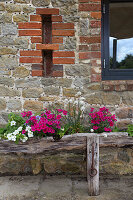 Blumenbeet aus rustikalem Holztrog vor Mauer aus Natursteinen und Ziegeln