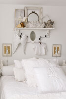 Old scatter cushions on bed below vintage-style decorations on shelf