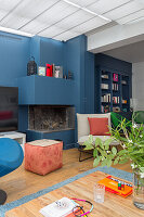 Sitzmöbel vor Kamin in offenem Wohnraum mit blauer Wand, im Hintergrund Bücherschrank