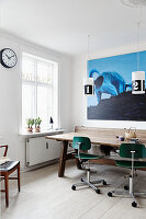 Solid wood dining table with green office chairs and artwork on the wall