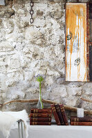Antique books and agapanthus in glass vase in front of rustic stone wall