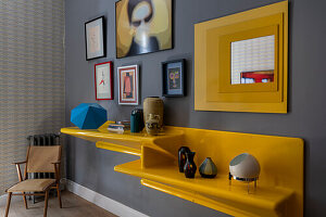 Yellow shelf with decorative objects and a gallery, on a grey wall in living room
