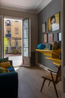 Gelbes Regal mit Dekoobjekten, darüber Gemälde an grauer Wand, Blick durch geöffnete Tür auf die Terrasse