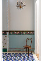 Thonet-Stuhl vor hellblauer Wand mit Fliesenbordüre im Sockelbereich