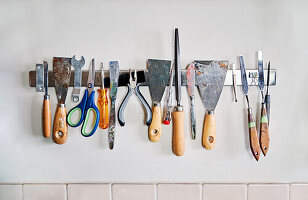 Palette knives and scissors with pliers and kit of professional instruments for artistic pottery placed on wall in workshop