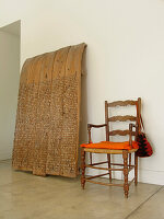 Wooden chair with blanket and handbag on concrete floor next to wooden sculpture