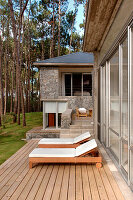 Sonnenliegen auf der Kiefernholzterrasse eines modernen Hauses aus Stein und Glas in einem Waldgebiet