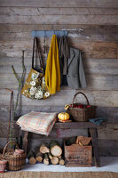 Rustikale Holzvertäfelung mit Garderobe, gefüllt mit Jacke, Schal und Pullover, einer Bank mit Kürbis und einer Decke und einem Korb mit roten Äpfeln