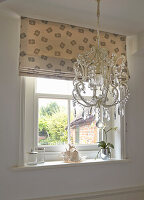 Chandelier in front of window with Roman shade