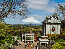 Sitting area outside tool shed in sunny garden with view of landscape