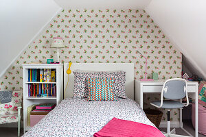 Children's room in the attic with floral wallpaper, bed and desk