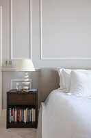 Bedside cabinet with books and table lamp next to bed in bedroom