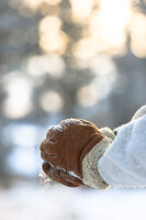 Hands in brown gloves forming a snowball, blurred winter background