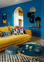 Living room with blue walls, yellow sofa and round mirrors