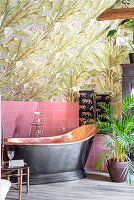 Freestanding copper bathtub with tropical wallpaper motif and pink tiles