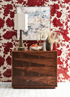 Chest of drawers in dark wood in front of floral wallpaper in red and white